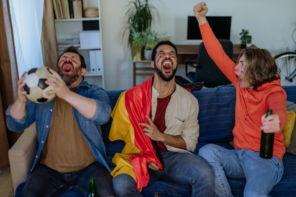 Happy German football fans friends watching football at home and eating the popcorn.