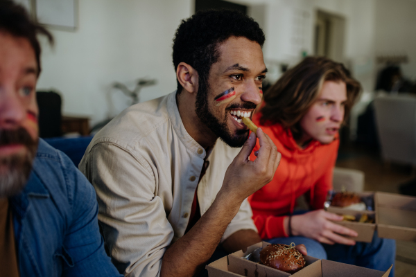 Nervous football fans friends staring at TV and watching football match at home.