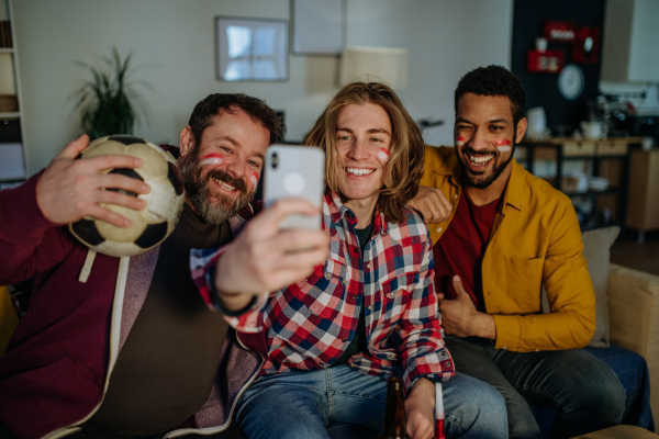 Happy football fans friends watching a football at home and taking selfie