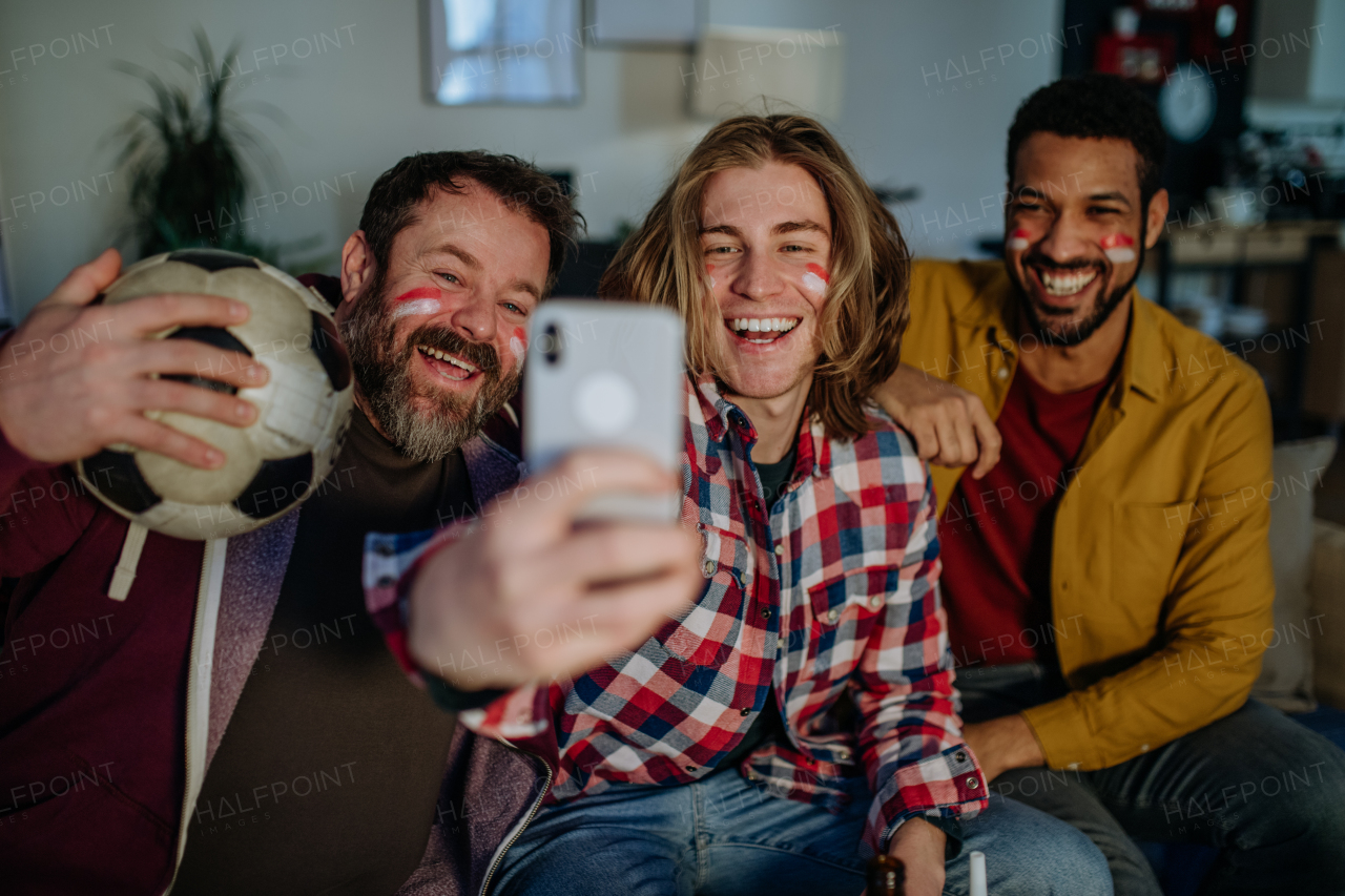 Happy football fans friends watching a football at home and taking selfie