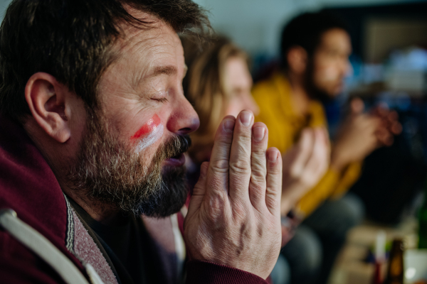 Nervous football fans friends watching match on a TV at home and praying.