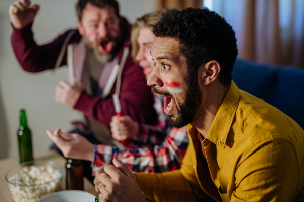 A close-up of excited football fan watching match with friends at home.