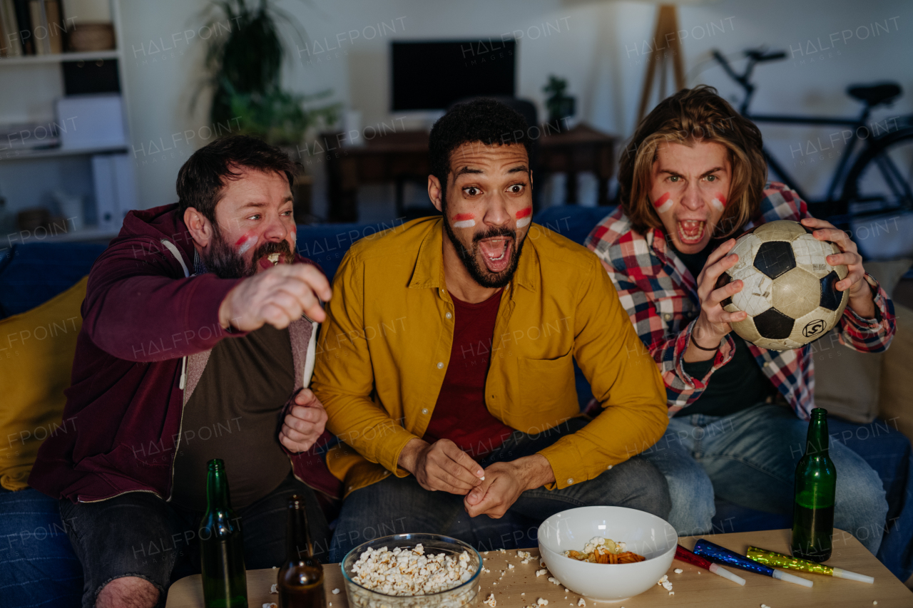 Nervous football fans friends watching live soccer match on a TV at home