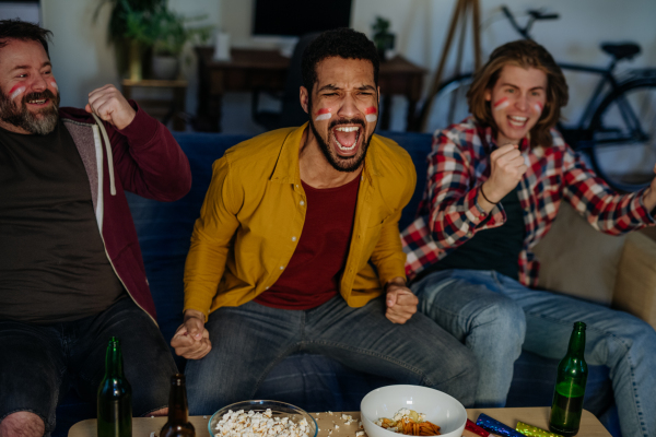 Happy German football fans friends watching football at home and eating the popcorn.