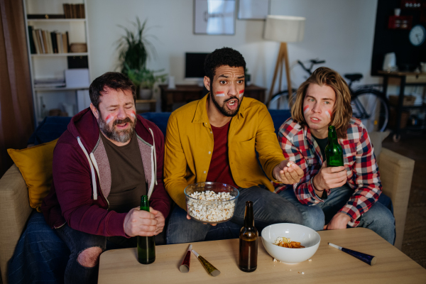 Nervous football fans friends watching live soccer match on a TV at home