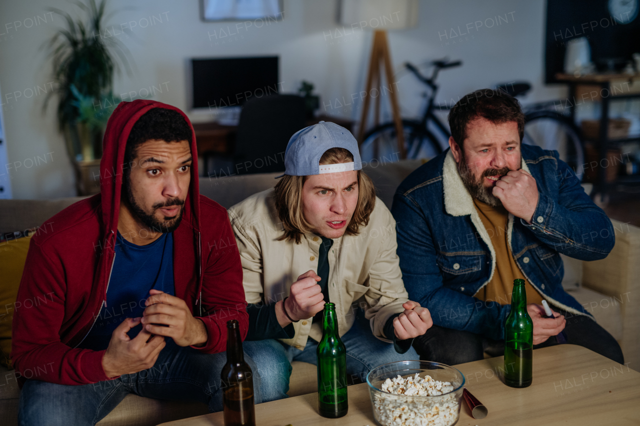 Nervous football fans friends watching live soccer match on a TV at home