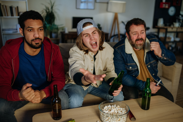 Nervous football fans friends watching live soccer match on a TV at home