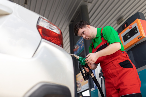 A Down syndrome man employee fueling car at gas station.