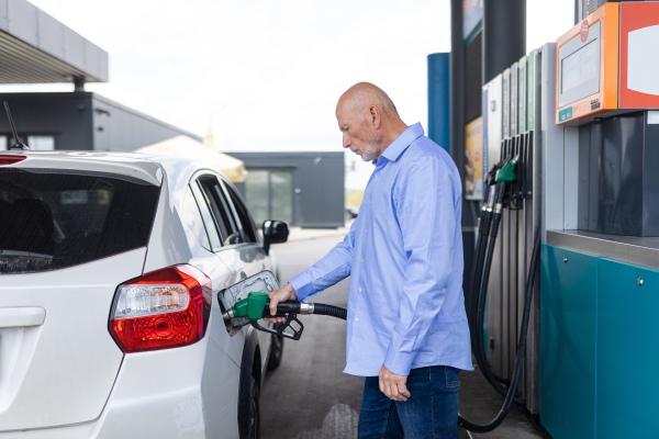 A senior businessman standing on gas station and fueling car.