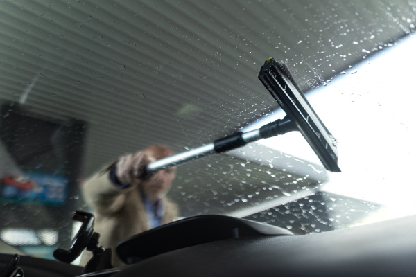 Close-up of senior businessman washing a car window at gas station.