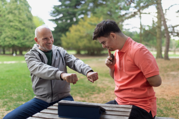 A happy senior father with his adult son with Down syndrome playing and sitting in park.