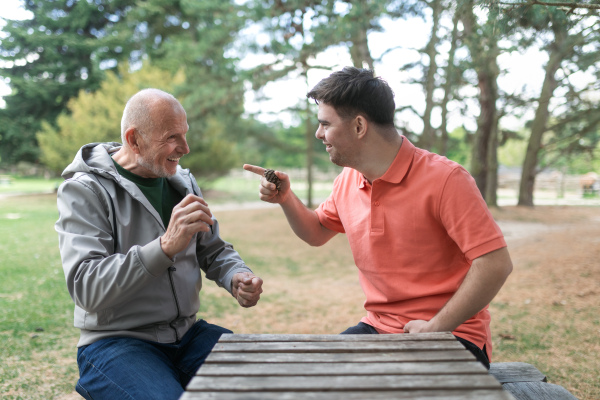 A happy senior father with his adult son with Down syndrome playing and sitting in park.