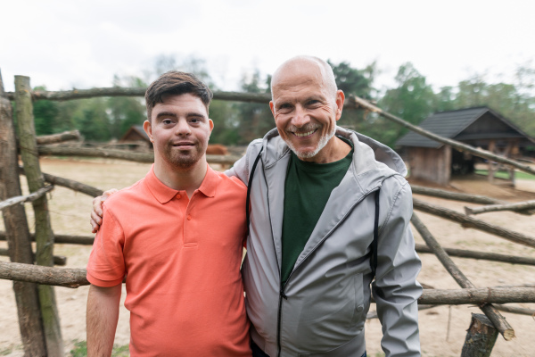 A happy senior father with his adult son with Down syndrome at ranch looking at camera.