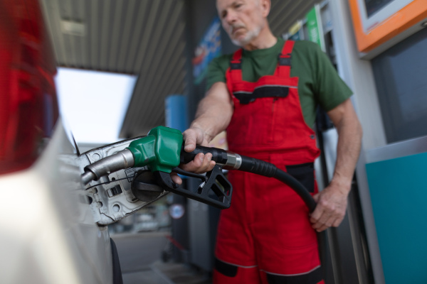 A senior worker standing on gas station and fueling car.