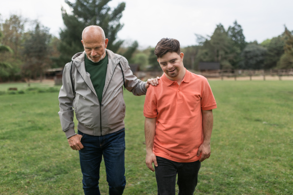 A happy senior father with his young son with Down syndrome walking in park together.