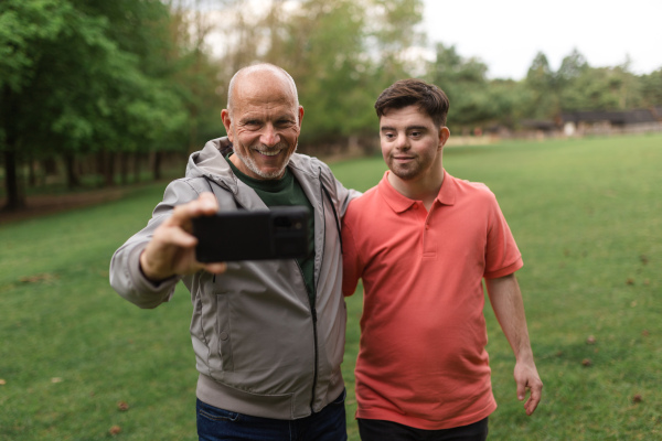 A happy senior father with his young son with Down syndrome taking selfie in park.