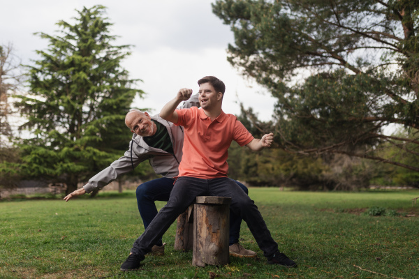 A happy senior father with his young son with Down syndrome sitting and having fun in park.