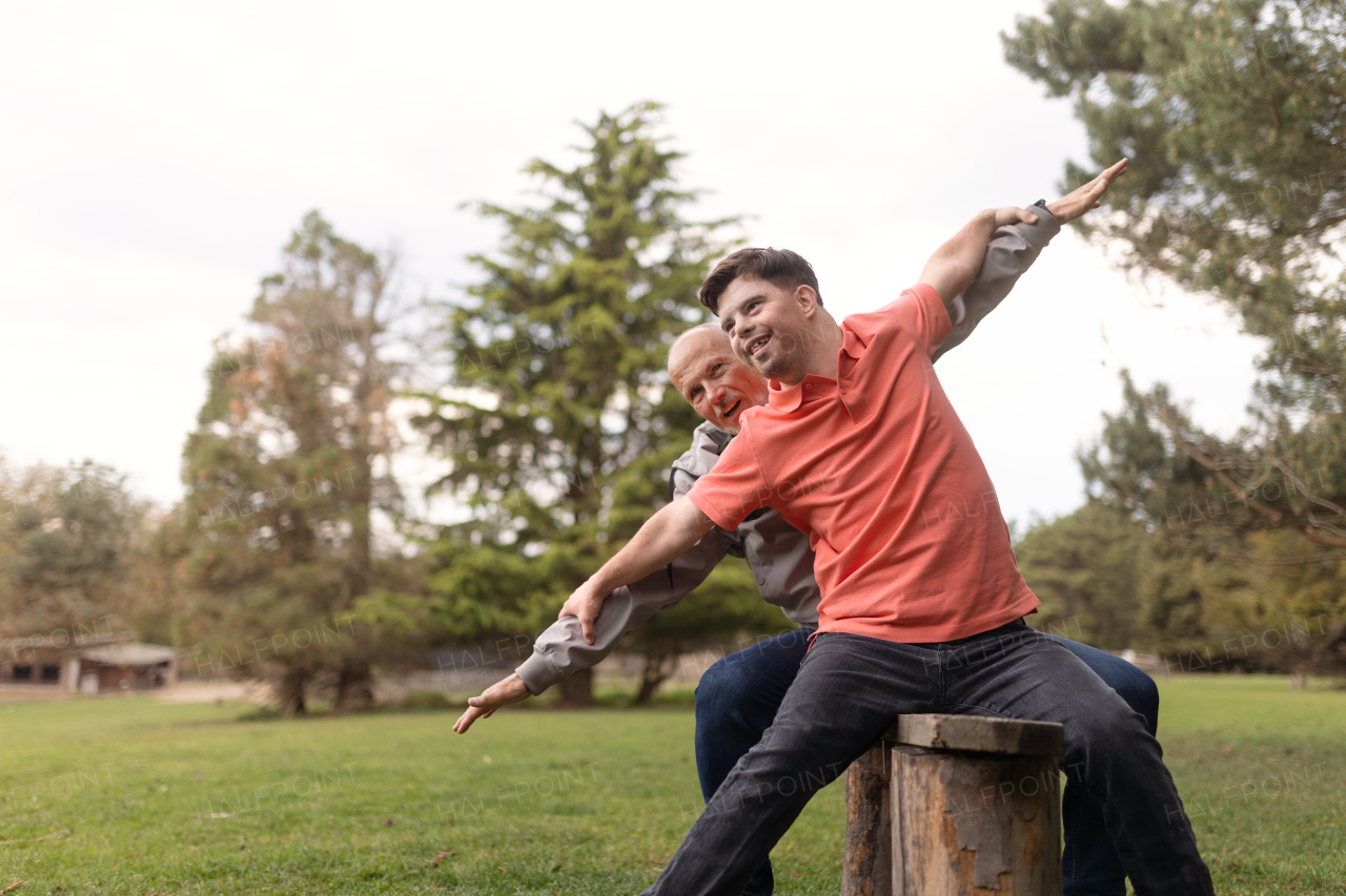 A happy senior father with his young son with Down syndrome sitting and having fun in park.