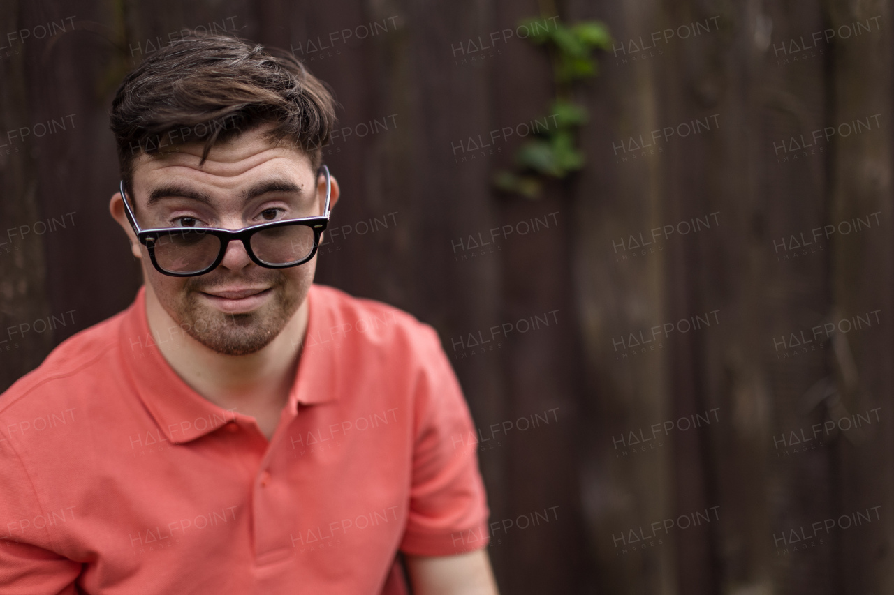 A portrait of happy young man with down syndrome standing outdoors in park and wearing sunglasses