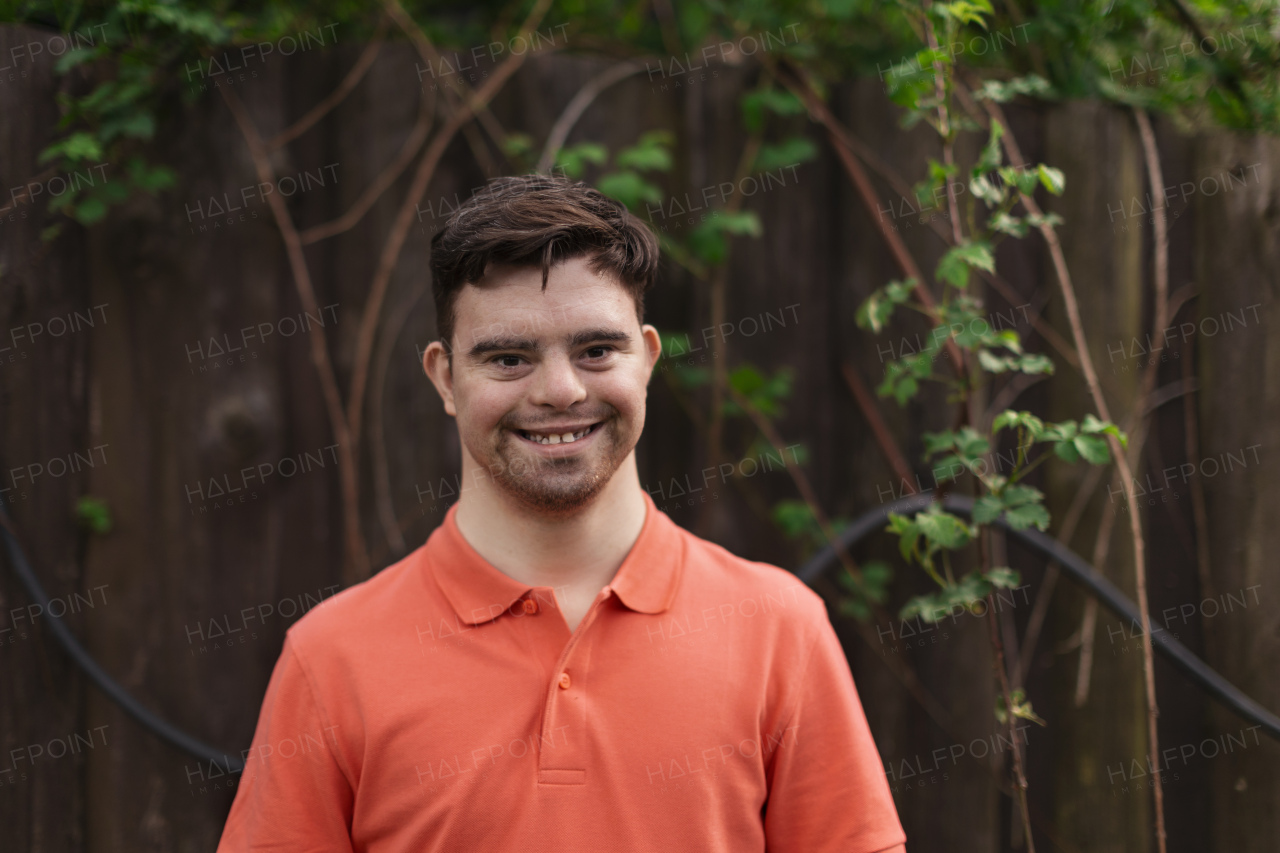 A portrait of happy young man with down syndrome standing outdoors in park