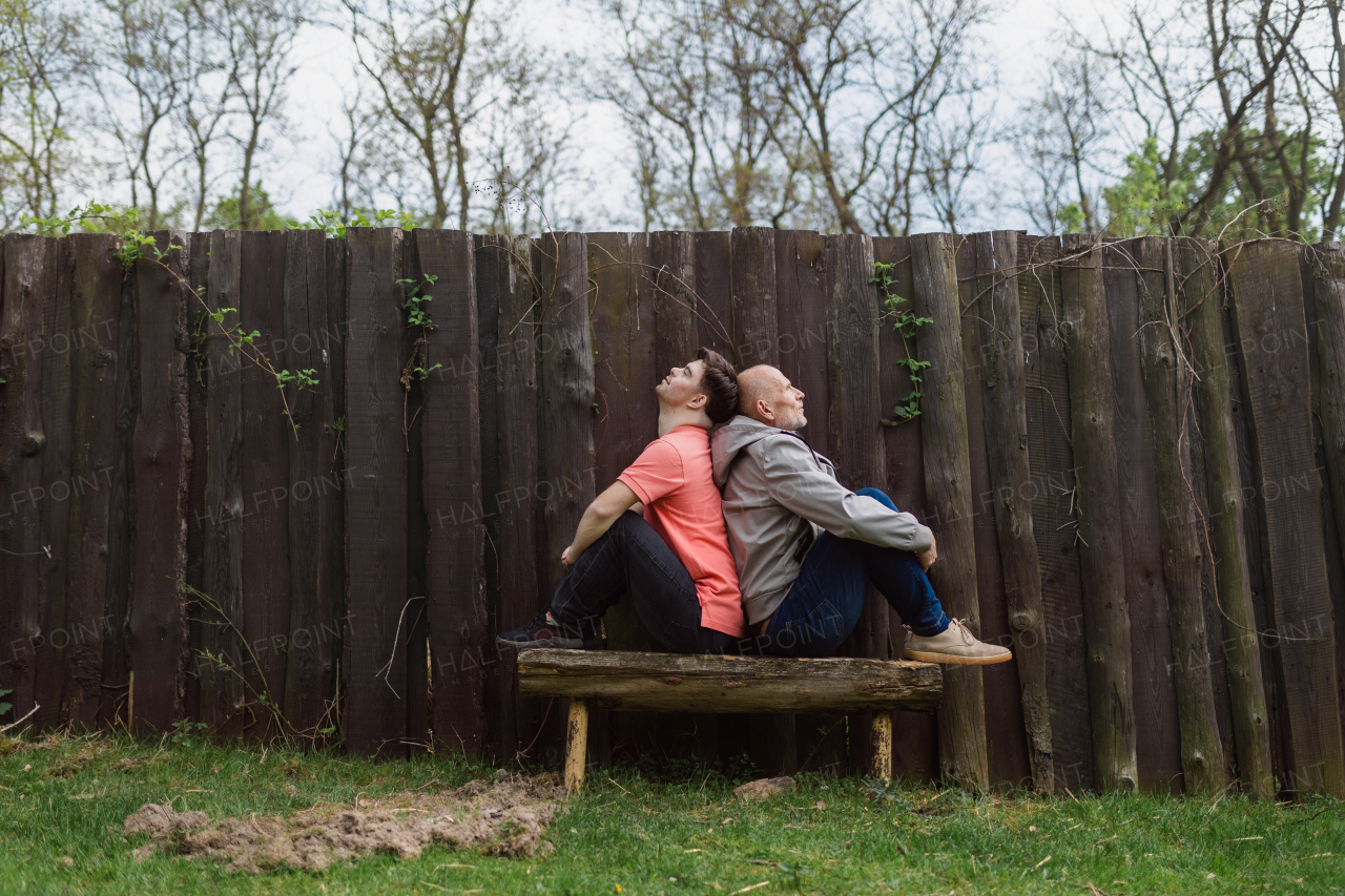 A happy senior father with his young son with Down syndrome sitting and having fun in park.