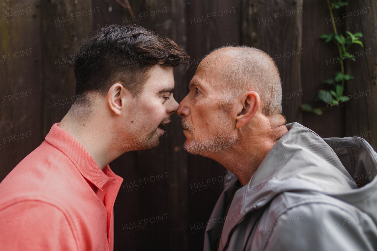 A portrait of happy senior father with his young son with Down syndrome outdoors.