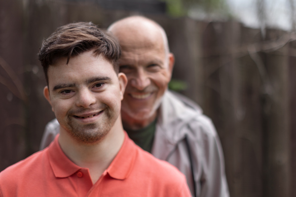 A portrait of happy senior father with his young son with Down syndrome outdoors.