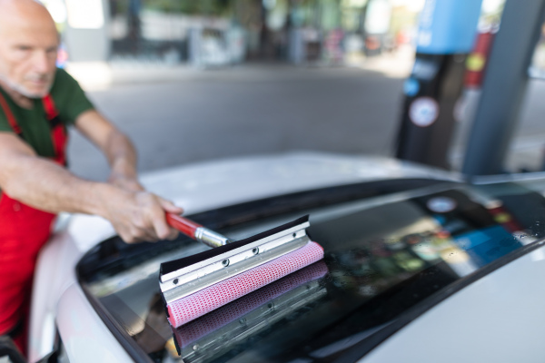 Senior worker washing a car window at gas station.