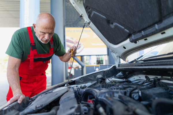 A senior mechanic checking the oil level in the car engine.