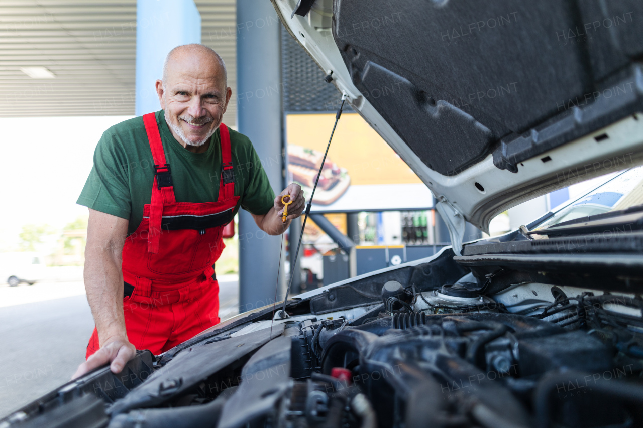 A senior mechanic checking the oil level in the car engine.