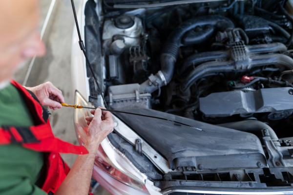 A senior mechanic checking the oil level in the car engine.