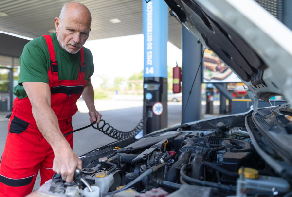 A senior mechanic checking the oil level in the car engine.