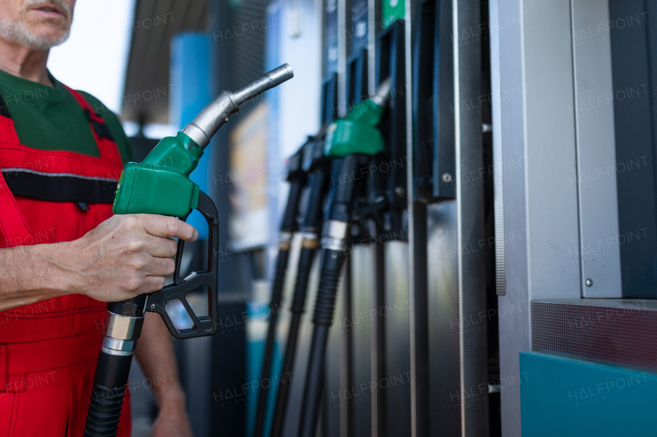 A senior worker standing on gas station and fueling car.