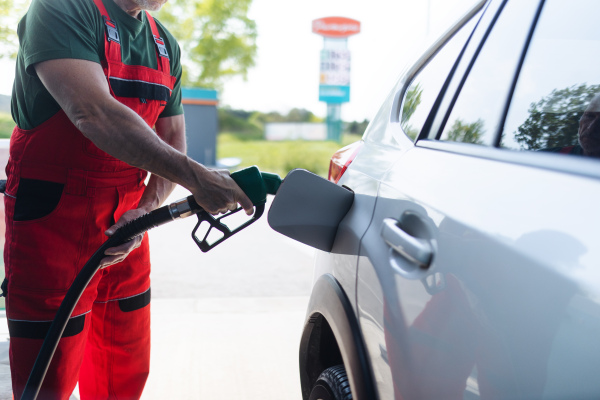 A senior worker standing on gas station and fueling car.