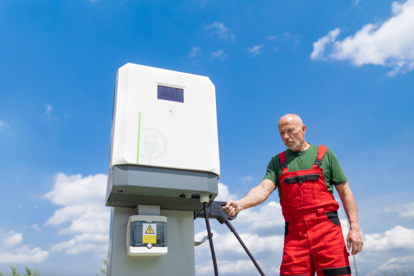 A senior worker standing on gas station and holding fueling pump.