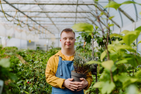 A happy young employee with Down syndrome working in garden centre, taking care of flowers.