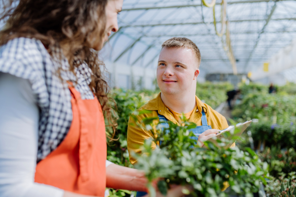 An experienced woman florist helping young employee with Down syndrome in garden centre.