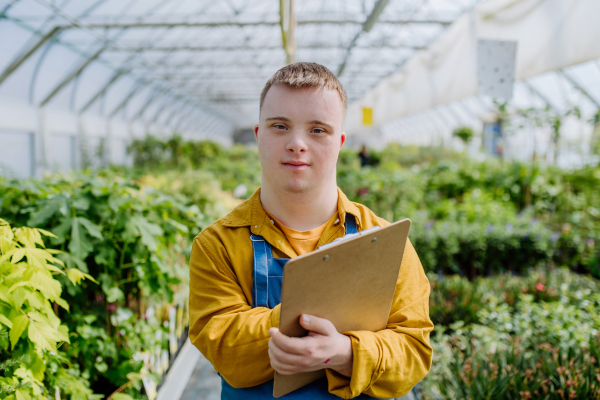 A young man with Down syndrome working in garden centre, holidng clipboard and checking plants.