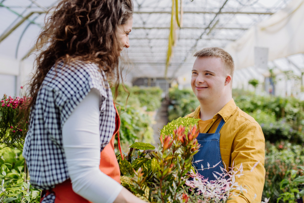 An experienced woman florist helping young employee with Down syndrome in garden centre.