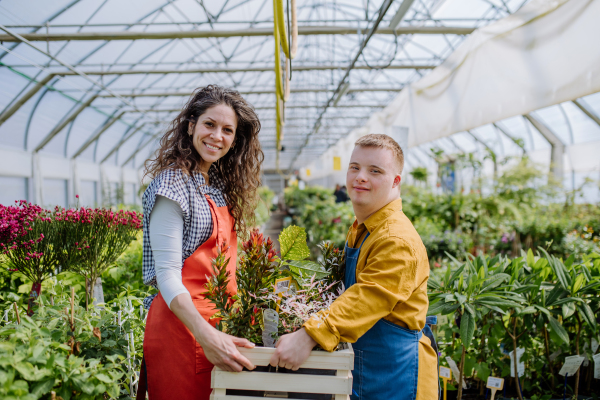 An experienced woman florist helping young employee with Down syndrome in garden centre.