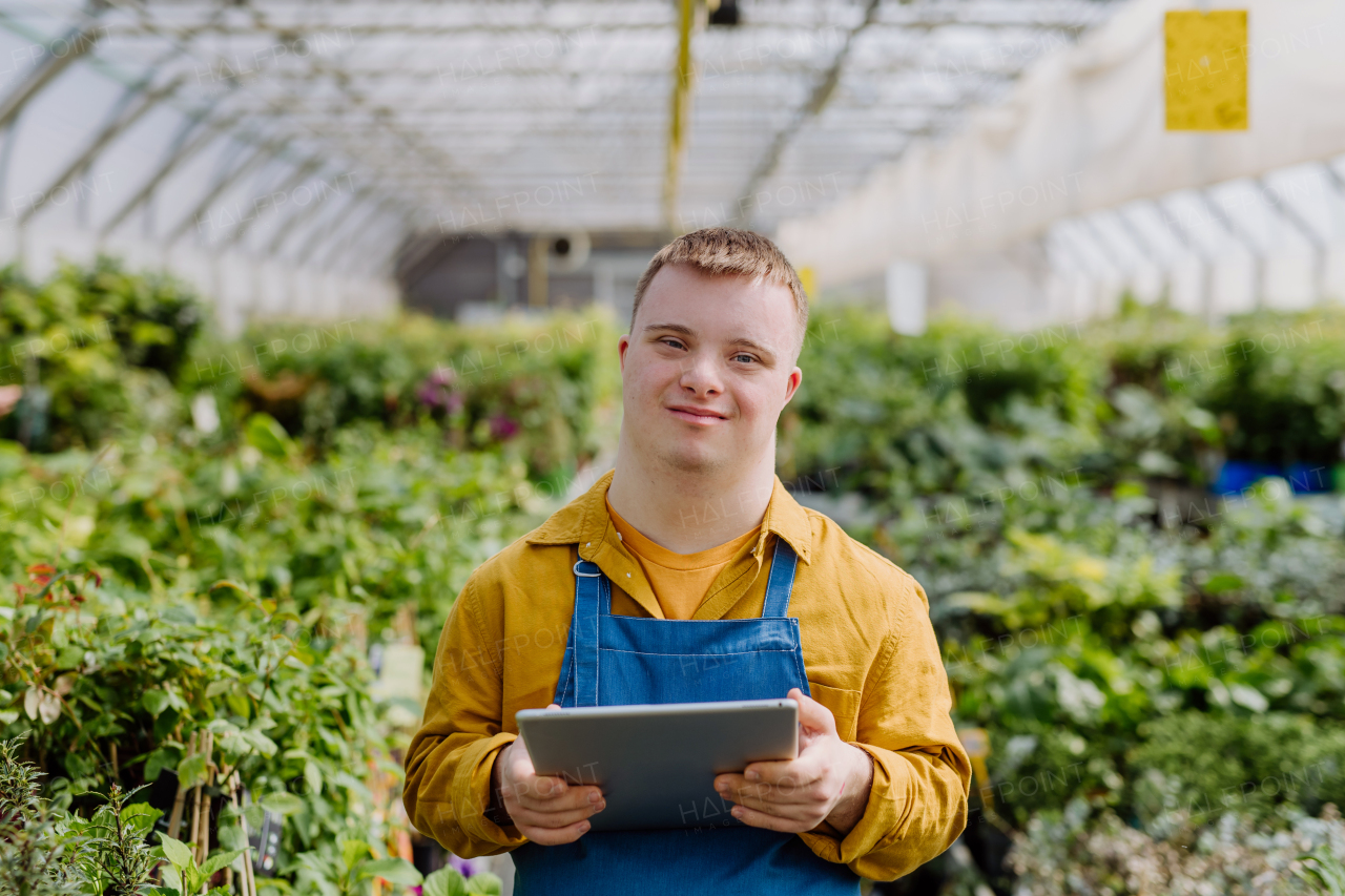 A young man with Down syndrome working in garden centre, holidng clipboard and checking plants.