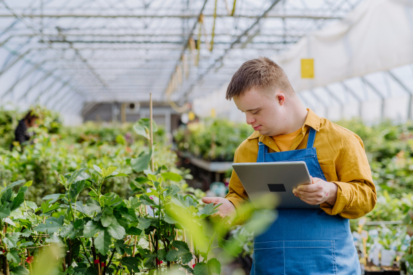 A young man with Down syndrome working in garden centre, holidng clipboard and checking plants.