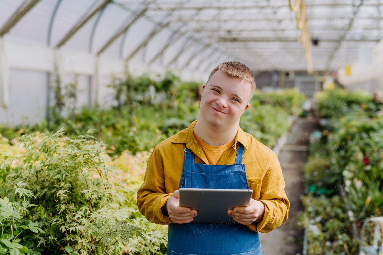 A young man with Down syndrome working in garden centre, holidng clipboard and checking plants.