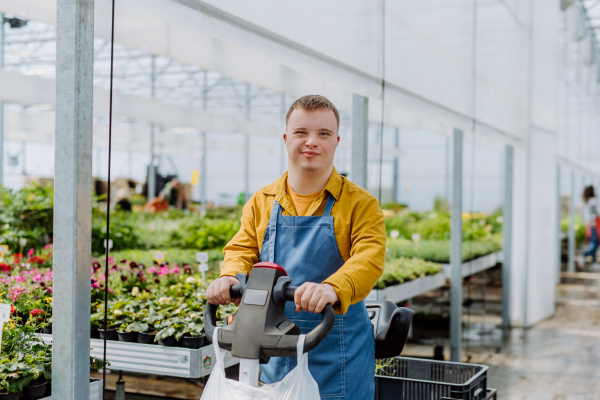 A young employee with Down syndrome working in garden centre, using hand pallet stacker.