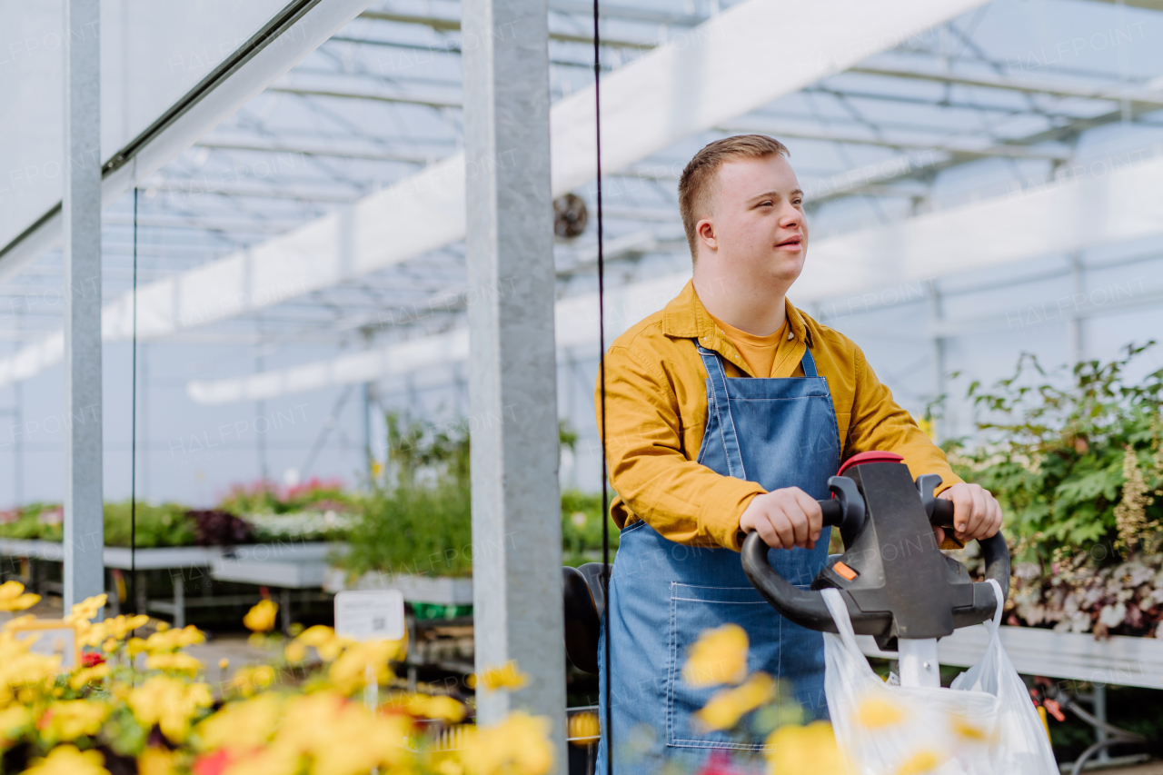 A young employee with Down syndrome working in garden centre, using hand pallet stacker.