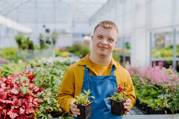 A happy young employee with Down syndrome working in garden centre, taking care of flowers.