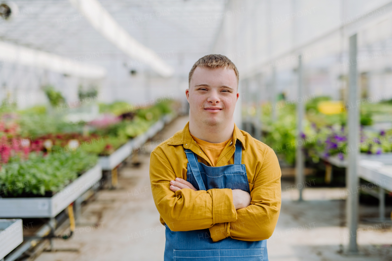 A young employee with Down syndrome working in garden centre, looking at camera with arms crossed.