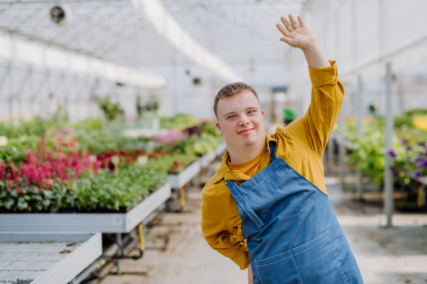 A young employee with Down syndrome working in garden centre, looking at camera and waving.