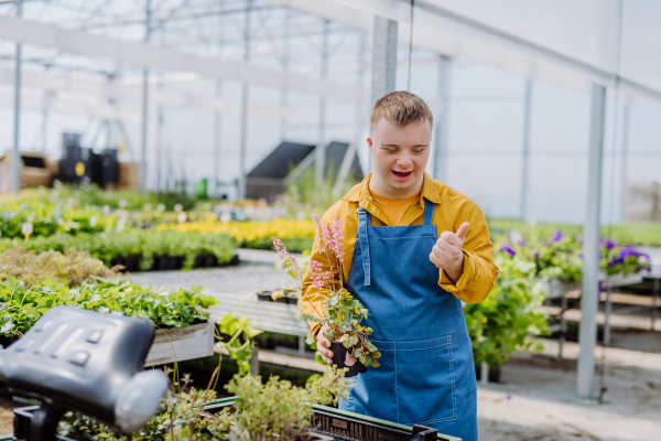 A happy young employee with Down syndrome working in garden centre, taking care of flowers.