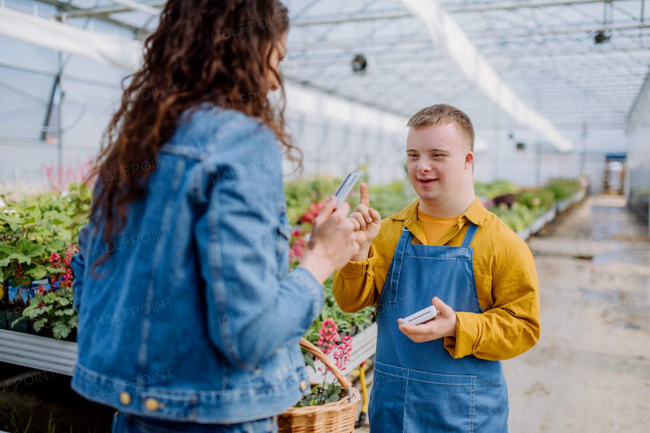 A happy young employee with Down syndrome working in garden centre, taking payment from customer.